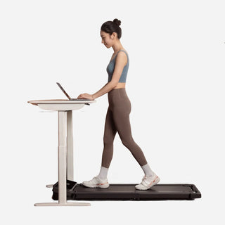 Woman walking on the WalkingPad Z3 Hybrid treadmill at a standing desk with the handrail folded down